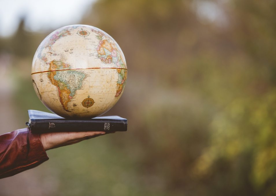 closeup-shot-person-holding-bible-with-desk-globe-top